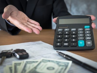 Car salesman holding a key and calculating a price at the dealership office